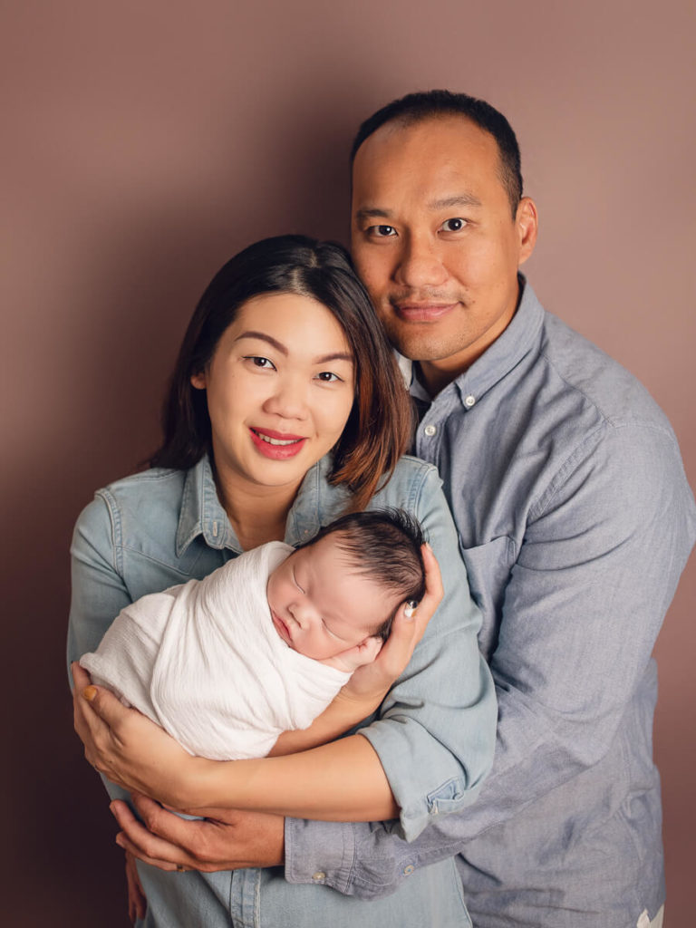 Swaddled baby with parents at newborn baby photos session