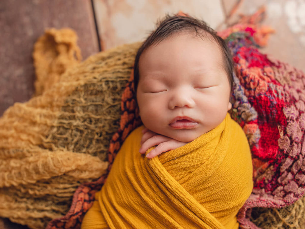 Colourful image featuring sleepy newborn boy wrapped in yellow.