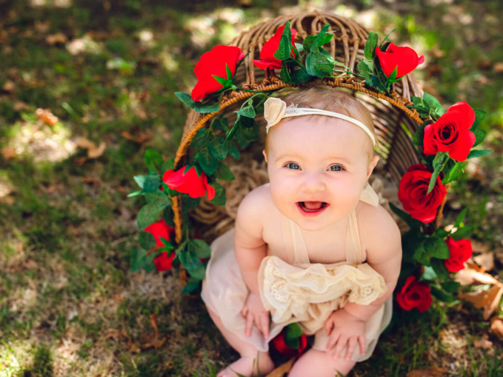 Happy, adorable older baby sitting in a cane seat for her photography session